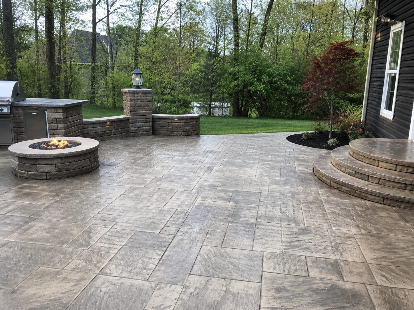Beautiful stamped concrete patio with fire pit, outdoor kitchen, and evening ambiance in Lee's Summit, MO
